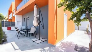Un edificio moderno con un comedor que incluye una mesa, sillas, un paraguas blanco y un pequeño árbol.