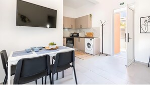 Una cocina moderna con televisor de pantalla plana, una mesa de comedor con sillas, lavadora y perchero.