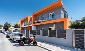 A modern two-story residential building with balconies, a gated driveway, and parked cars.