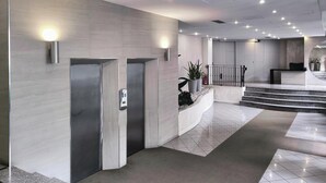 A modern hotel lobby with a reception desk, two elevators, and a staircase leading to another floor. - JOIVY Studio Near Pinacoteca Brera (Milan)