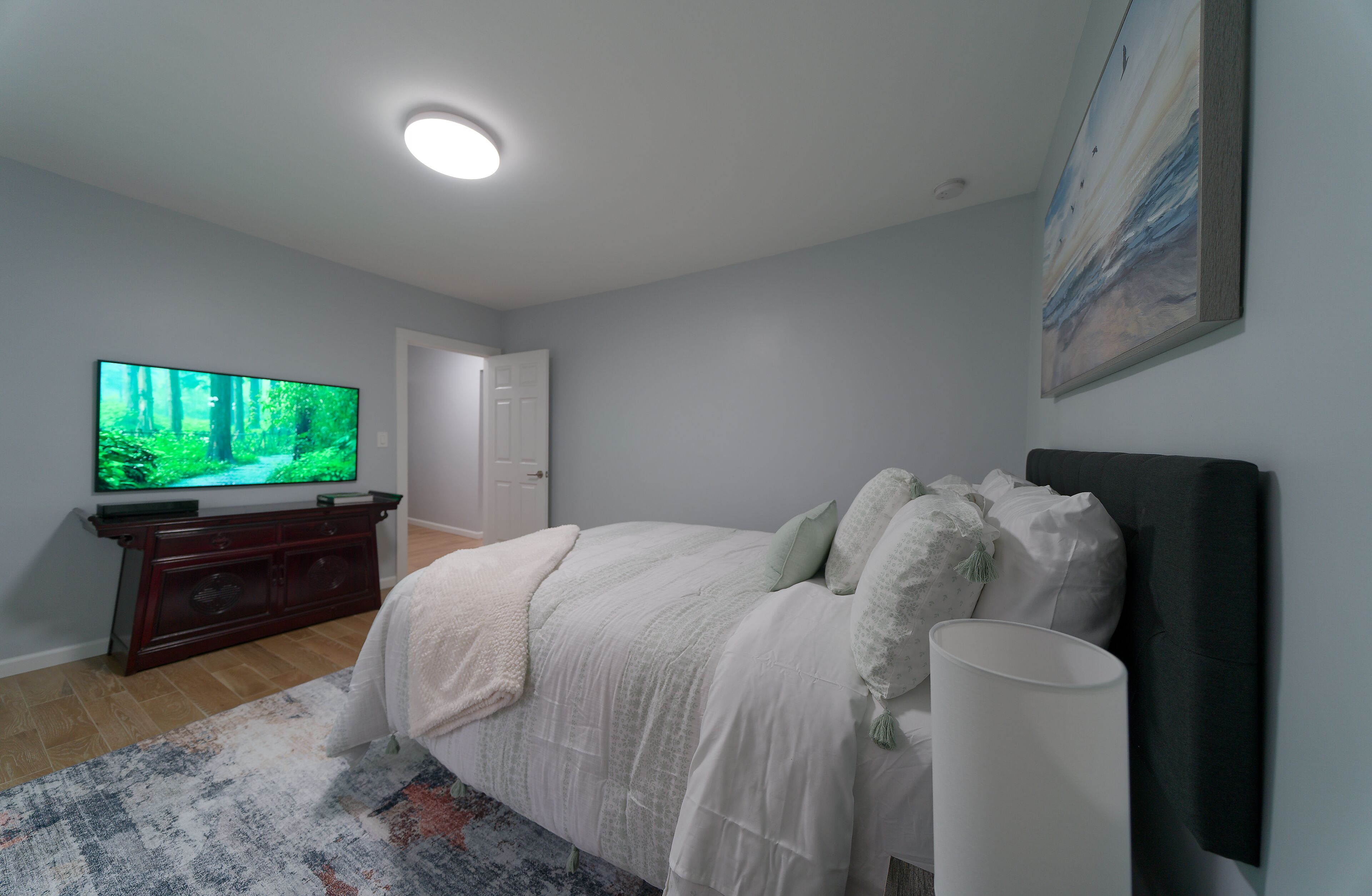 A bedroom with a bed, a television, and a painting on the wall.