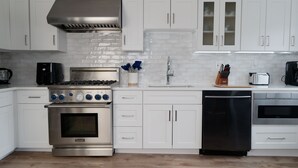 A modern kitchen with white cabinetry, a stainless steel stove, a dishwasher, and a tiled backsplash.