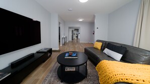 A modern living room with a flat-screen TV, a black coffee table, a sofa with cushions, and a yellow throw blanket.
