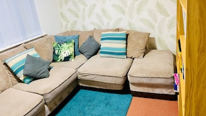 A cozy living room with a sofa set, a blue rug, and a bookshelf.