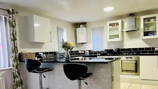 A modern kitchen with white cabinets, black countertops, and two black bar stools.