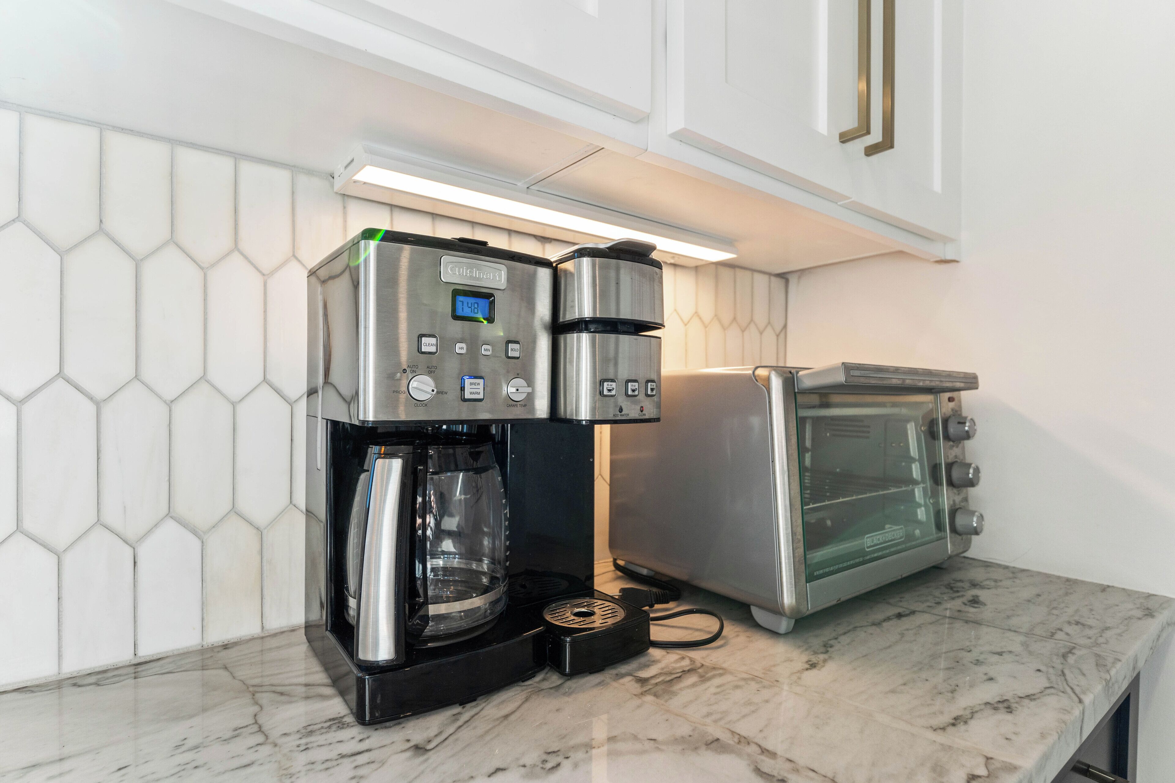 A kitchen with a coffee maker, toaster, and a hexagonal tiled backsplash.