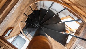 Un escalier en colimaçon avec des poutres en bois et des rampes en métal, menant à l’étage supérieur.
