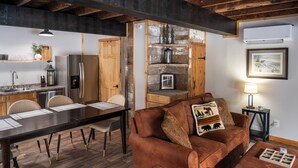 Un salon chaleureux avec un canapé marron, une table à manger avec des chaises, un coin cuisine avec un réfrigérateur et une cheminée agrémentée d’objets décoratifs.