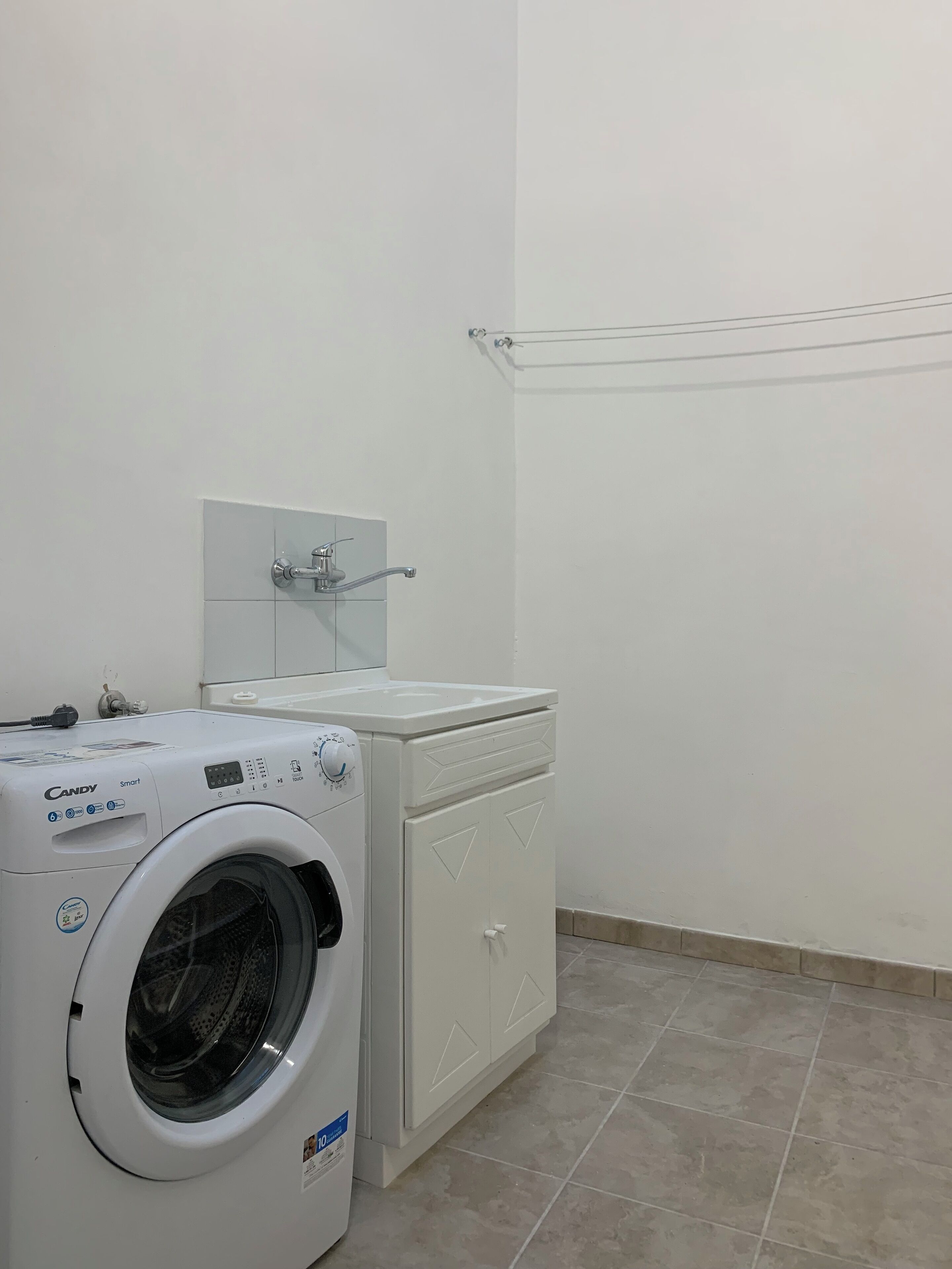 Un espace buanderie compact comprenant un lave-linge à chargement frontal et un sèche-linge, un sol carrelé et un porte-serviettes fixé au mur.