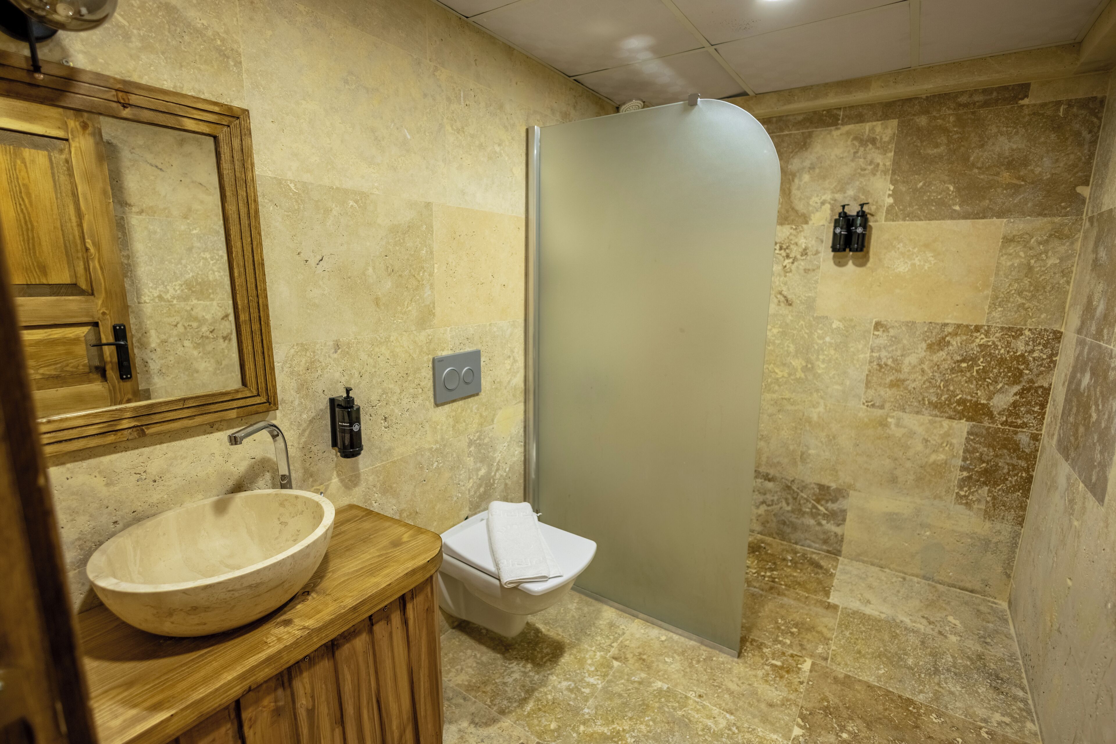 A bathroom with a wooden vanity, a large sink, a toilet, and a shower enclosure.