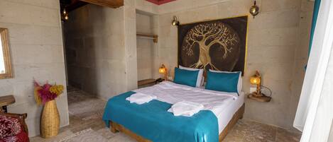 A bedroom with a wooden ceiling, a bed with teal bedding, a wall-mounted painting of a tree, and two bedside lamps.