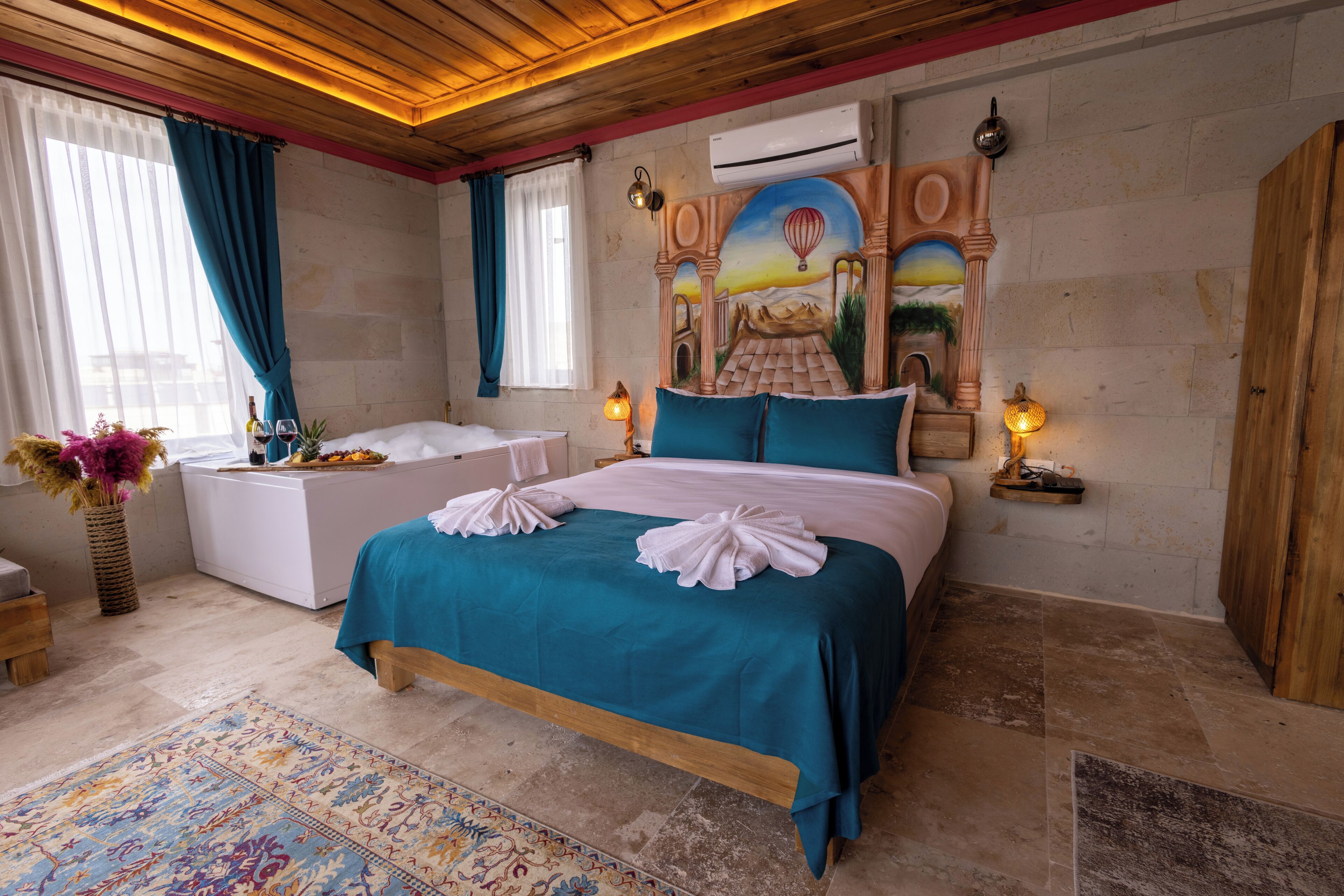 A bedroom with a bed, a nightstand, a lamp, a vase with flowers, and a wall mural.