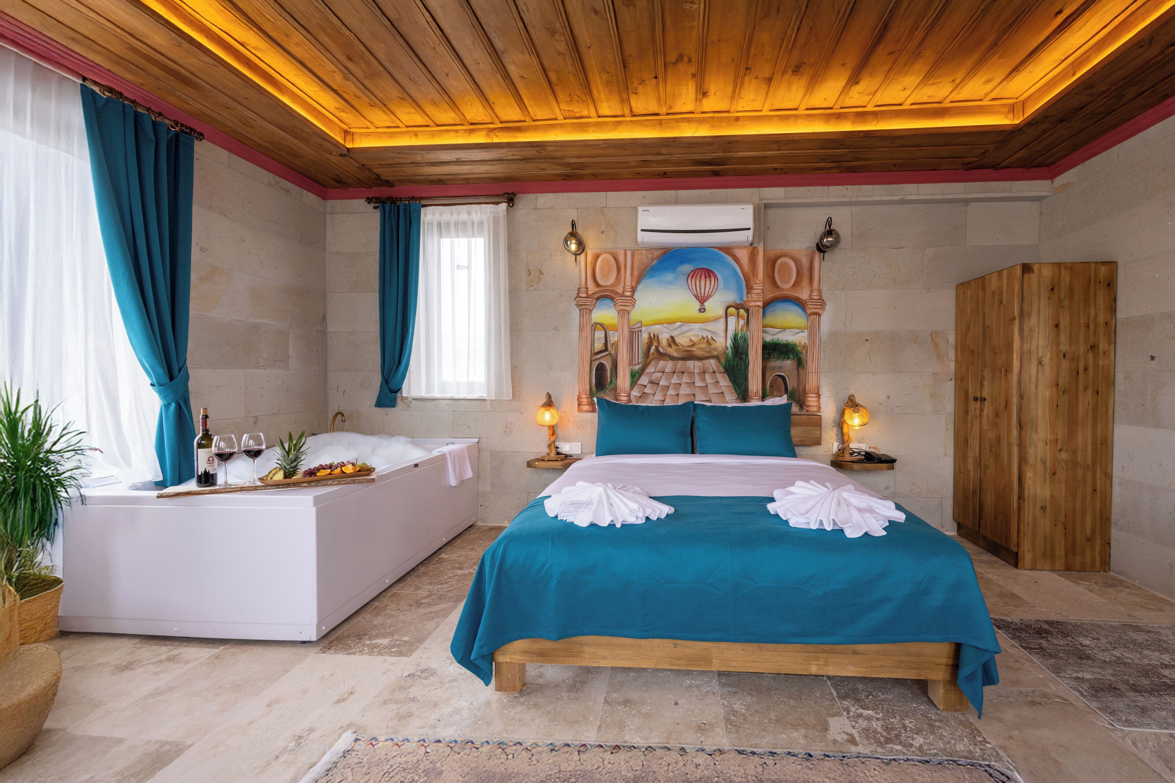 A bedroom with a large bed, a separate sitting area, a bathtub, and a wooden ceiling.