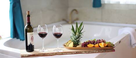 A bathtub with a tray of fruit and wine glasses.