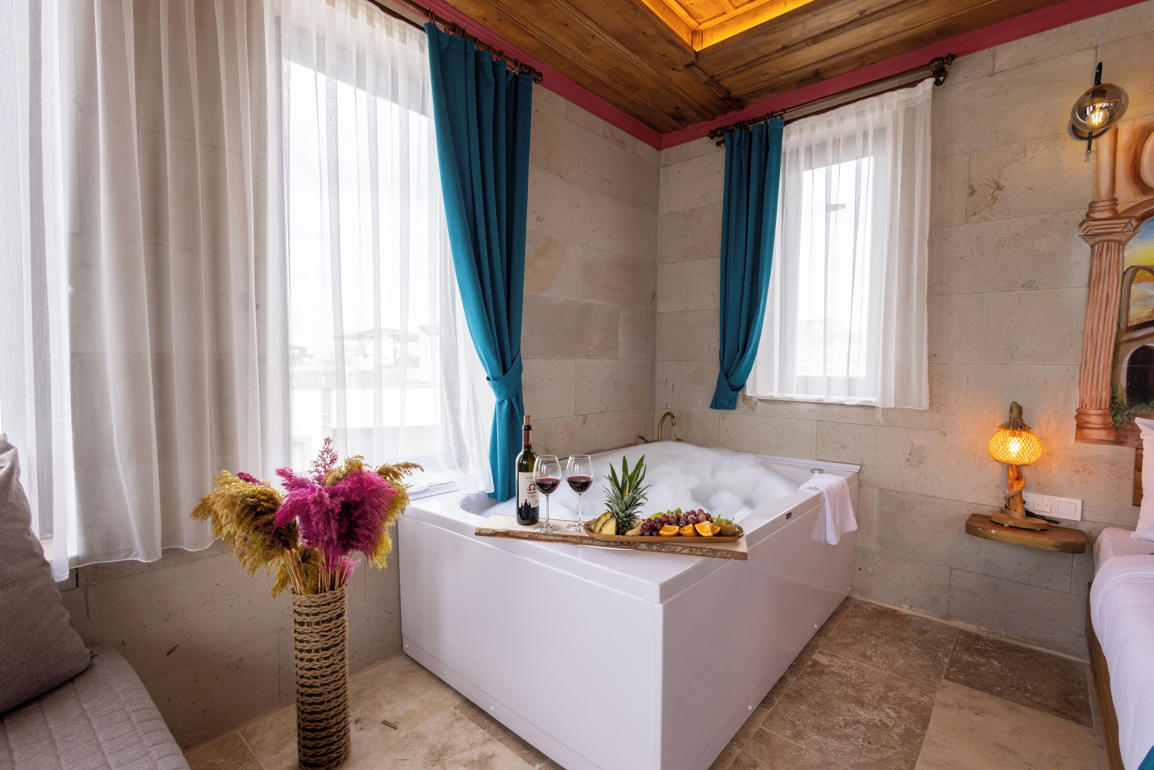 A modern bathroom with a bathtub, a wooden ceiling, and a stone wall.