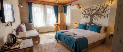 A bedroom with a wooden ceiling, a bed with blue bedding, a nightstand with a kettle, and a wall-mounted TV.