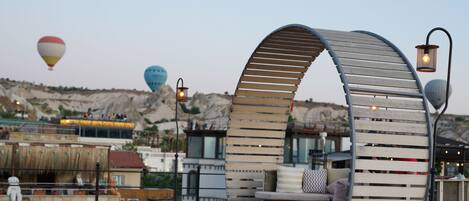 Una terraza en la azotea con un banco de madera curvo, un pequeño escenario y una zona de estar con cojines.