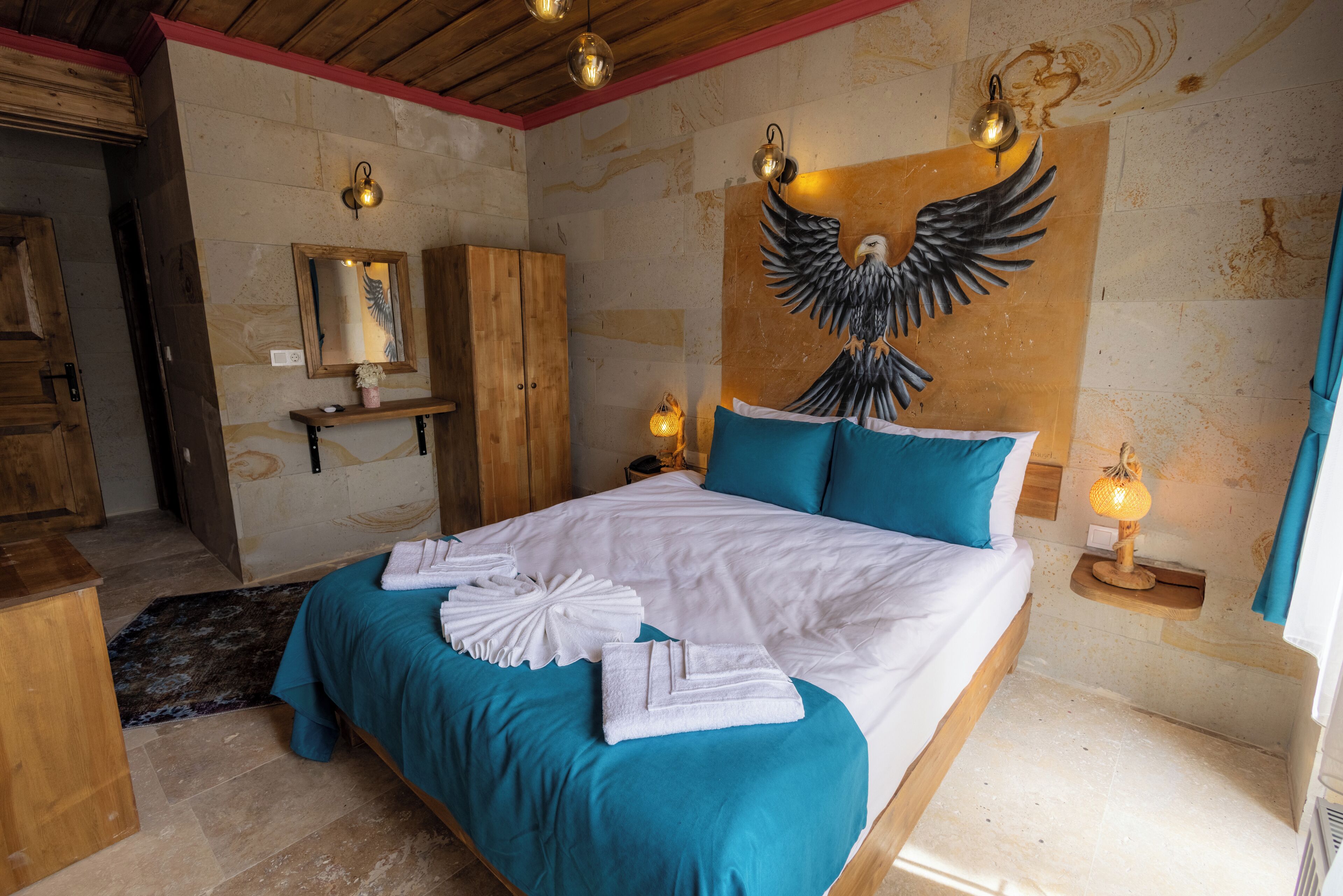 A bedroom with a large bed, a wooden wardrobe, a mirror, and a wall-mounted decorative piece.