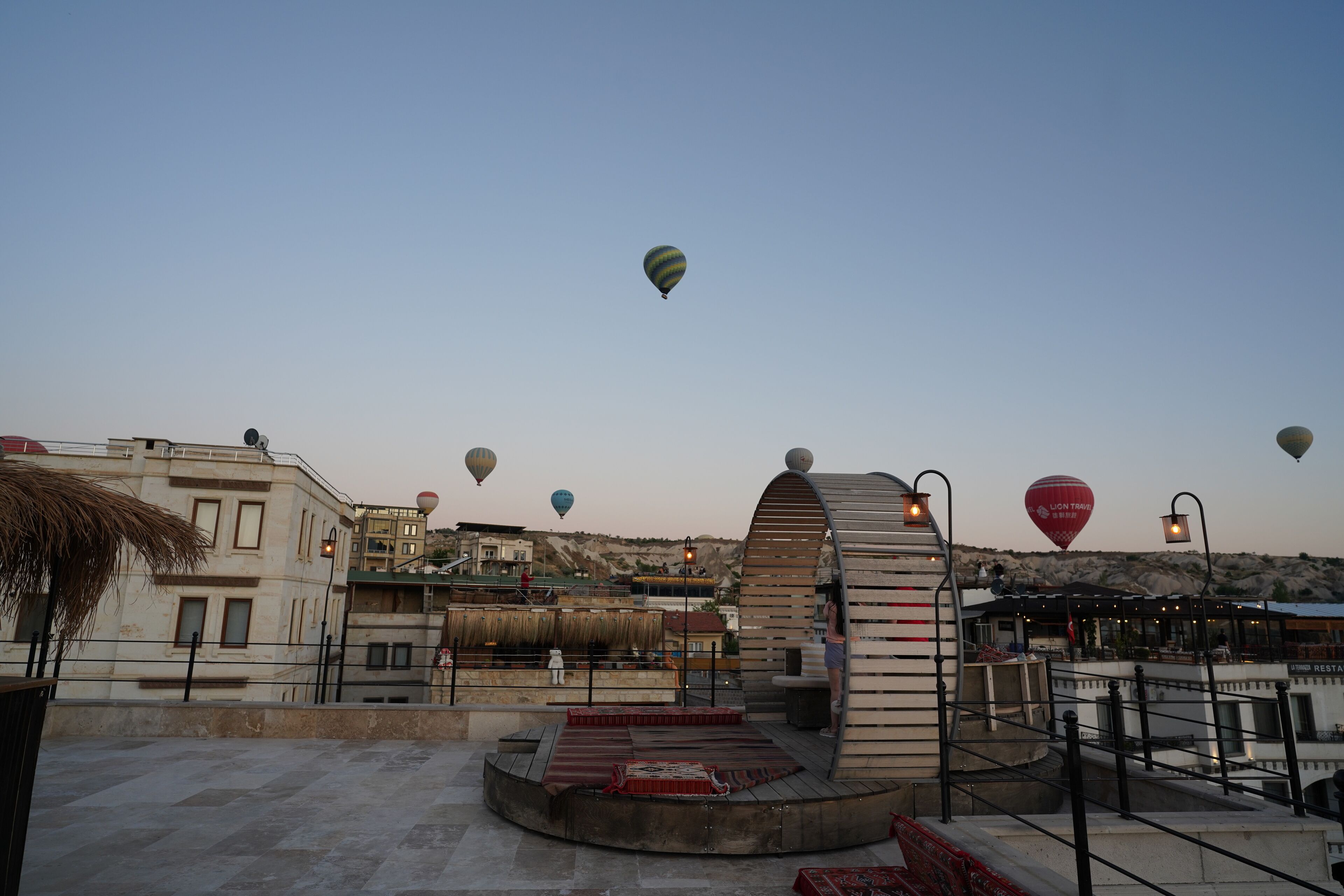 A rooftop terrace with a view of the cityscape and hot air balloons in the sky.