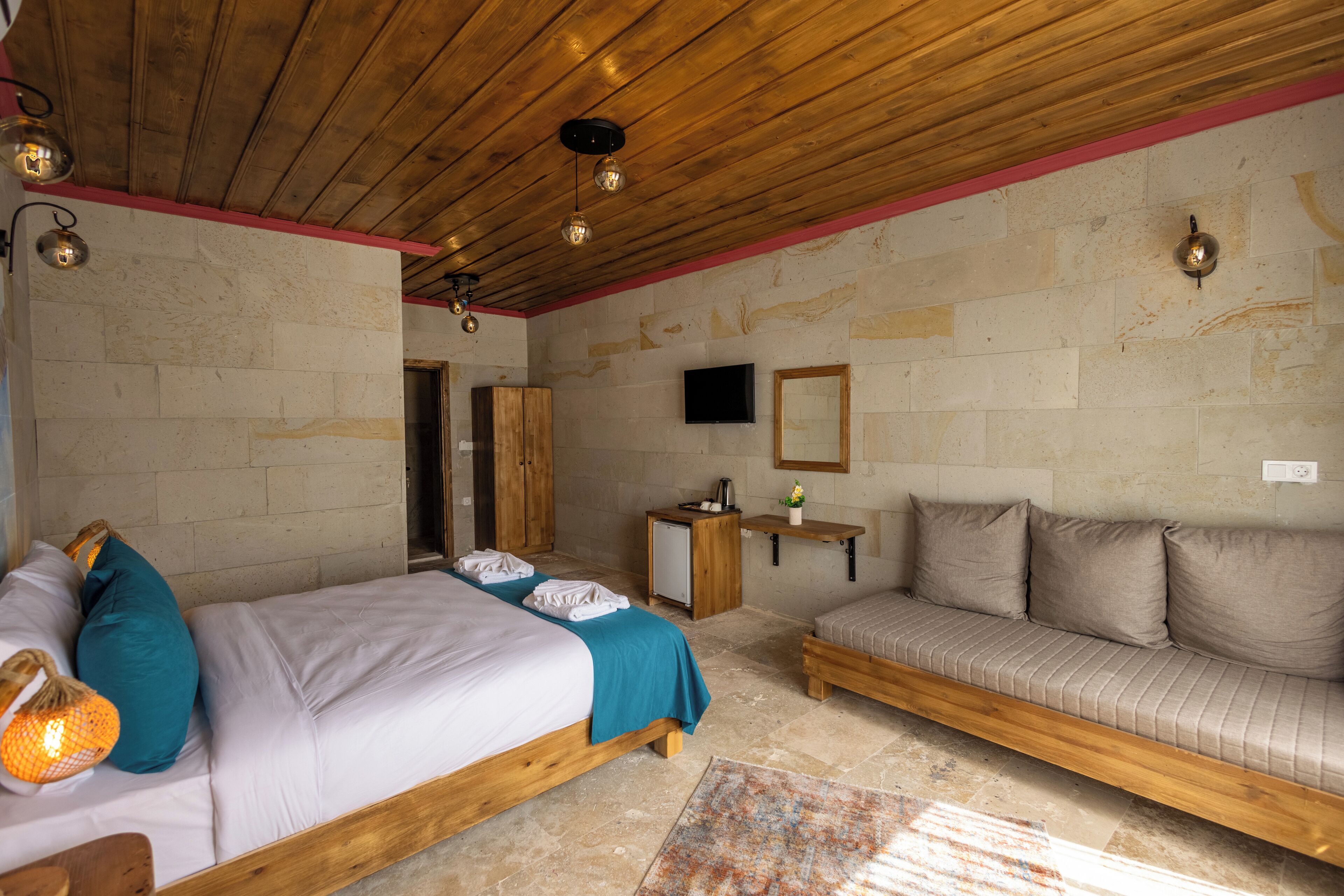 A bedroom with a bed, a sofa, a wooden ceiling, and a stone wall.