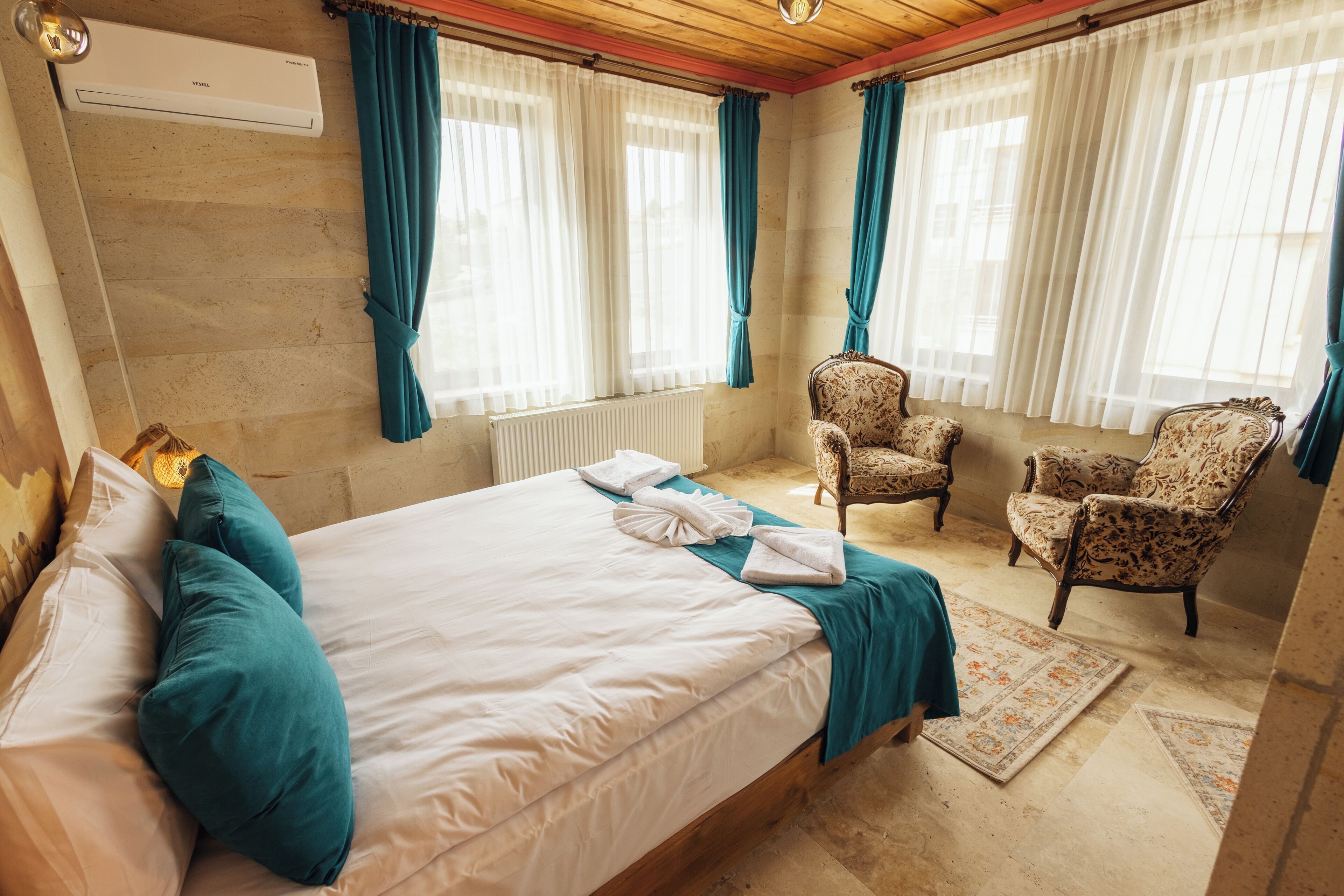 A hotel room with a bed, two chairs, a radiator, and curtains.