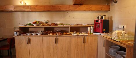 A kitchen with wooden cabinets, a countertop with various food items, a red refrigerator, and a chair.