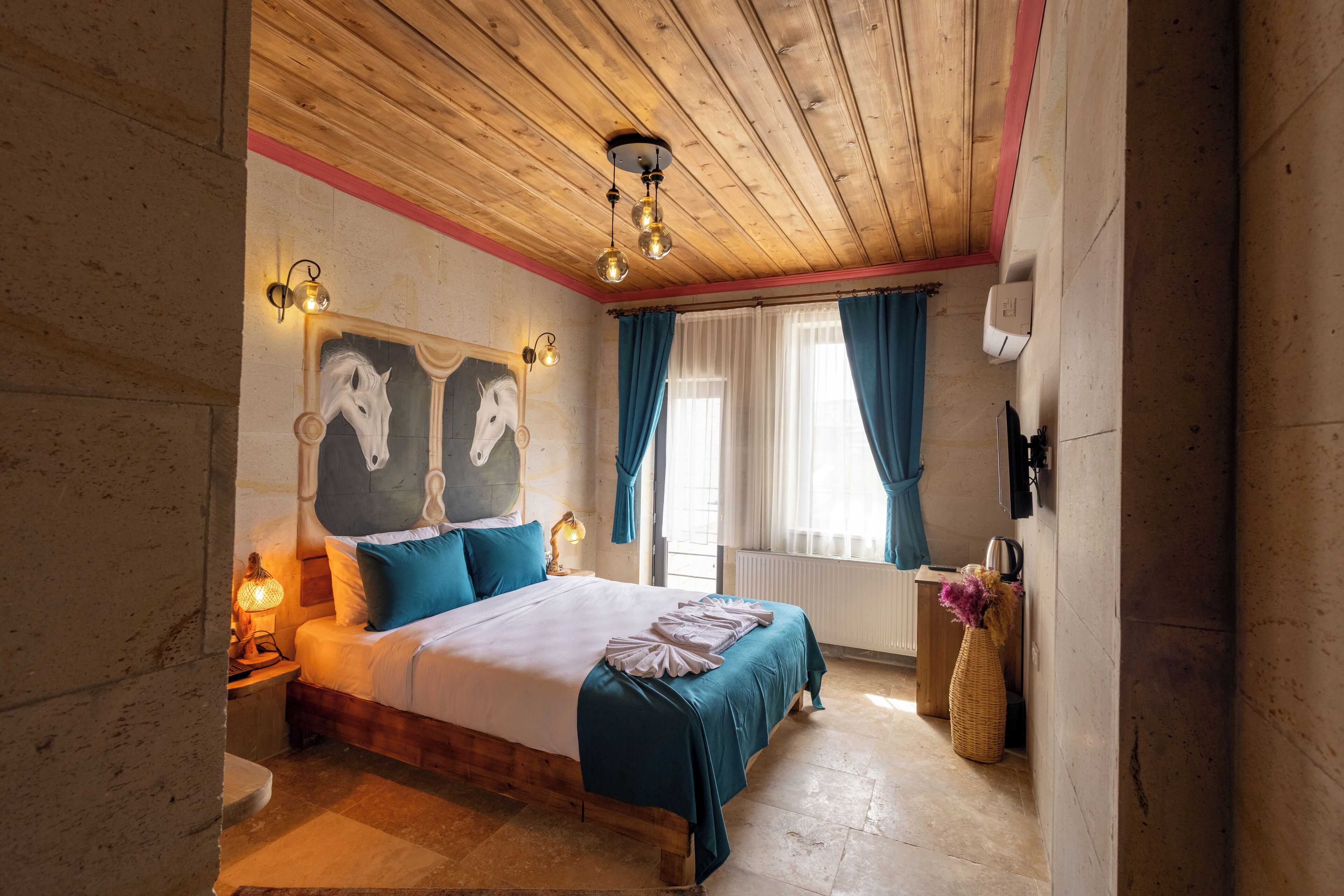 Une chambre confortable avec un plafond en bois, un grand lit avec une literie bleue, une table de chevet avec une lampe et des œuvres d’art accrochées au mur.