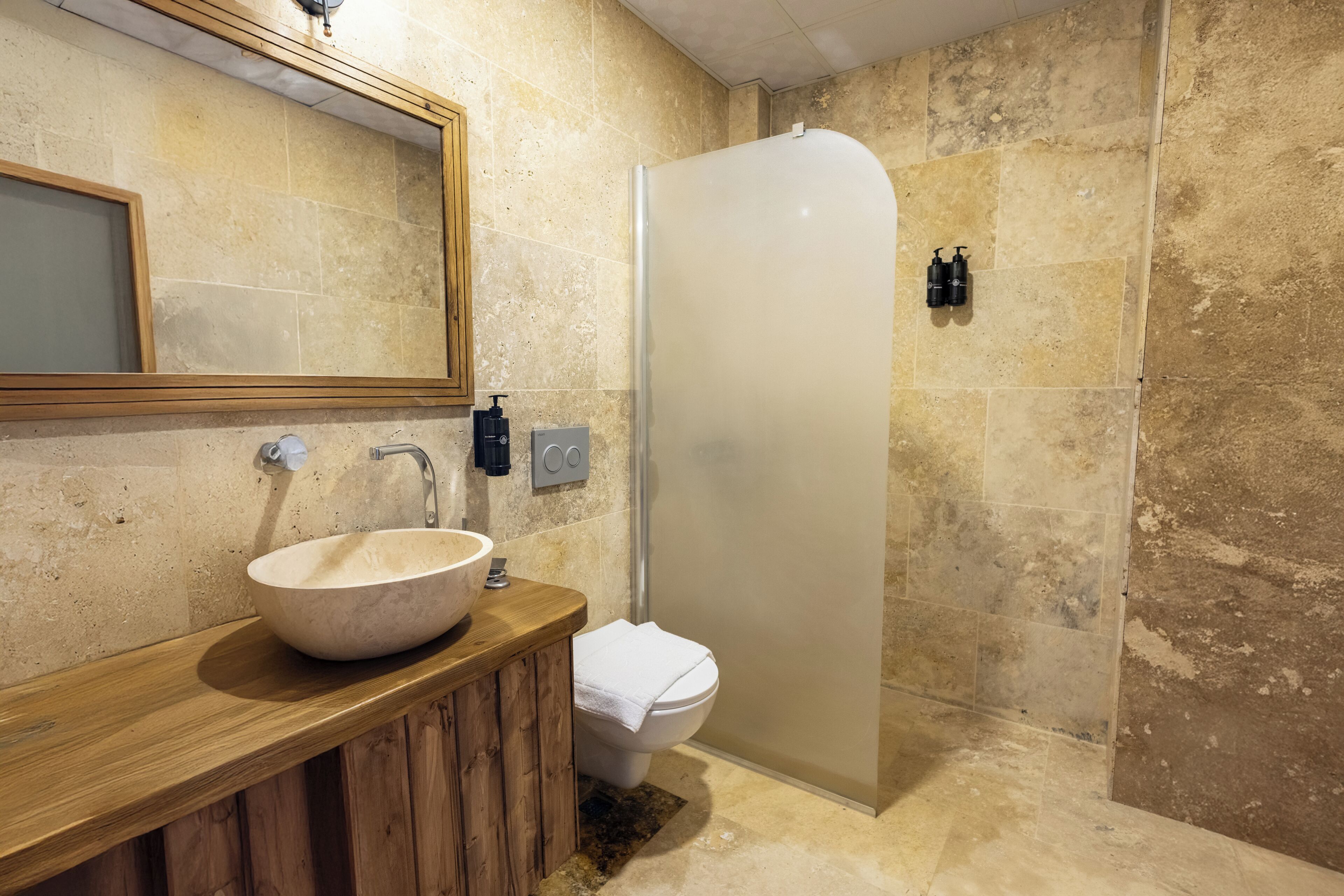 A bathroom with a wooden vanity, a large sink, a toilet, and a frosted shower enclosure.