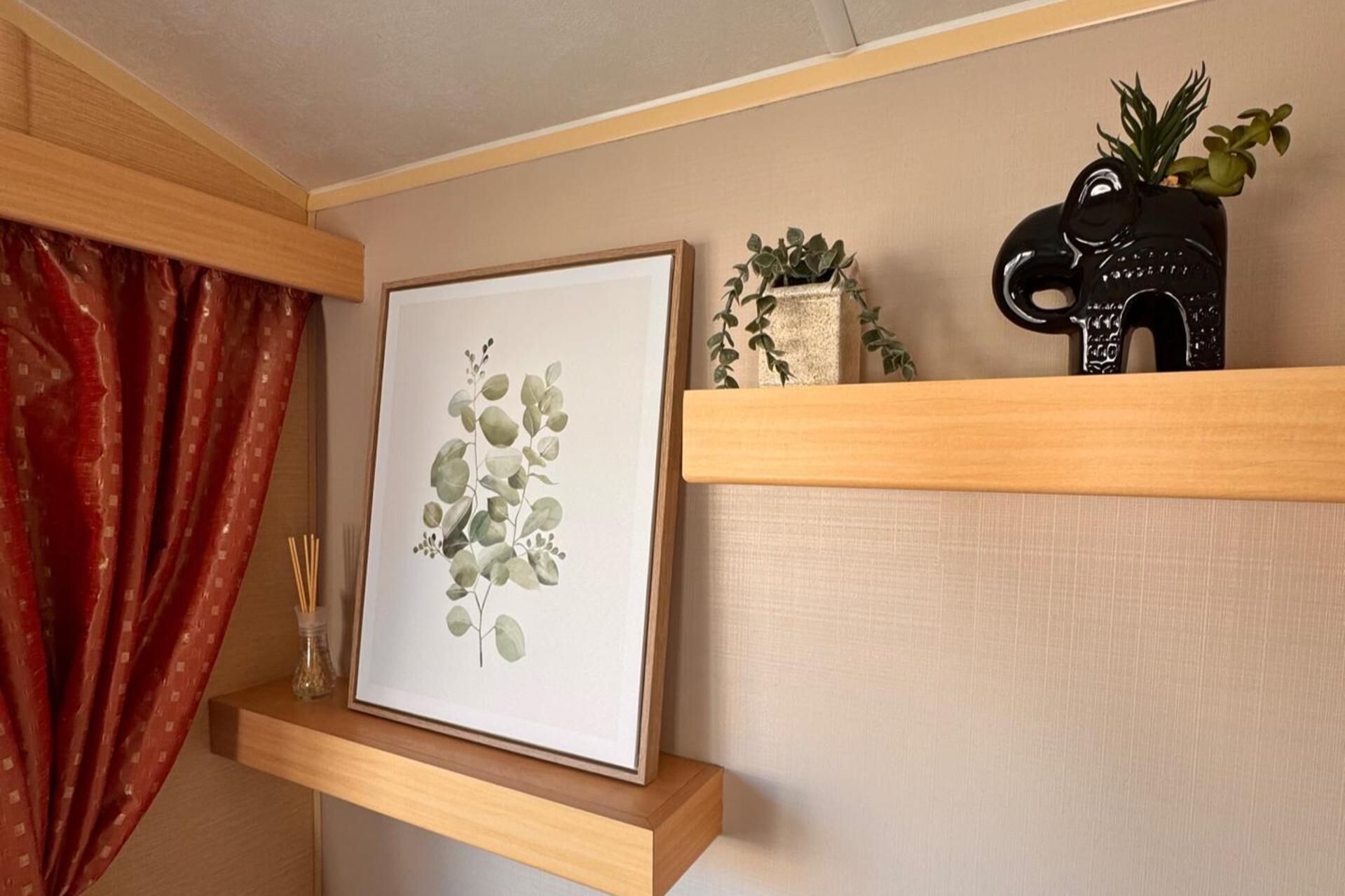 A framed botanical print on a wooden shelf, a small vase with green plants, and a black elephant-shaped object.
