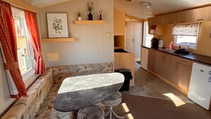 Interior compacto de una caravana con comedor, kitchenette y sofá.