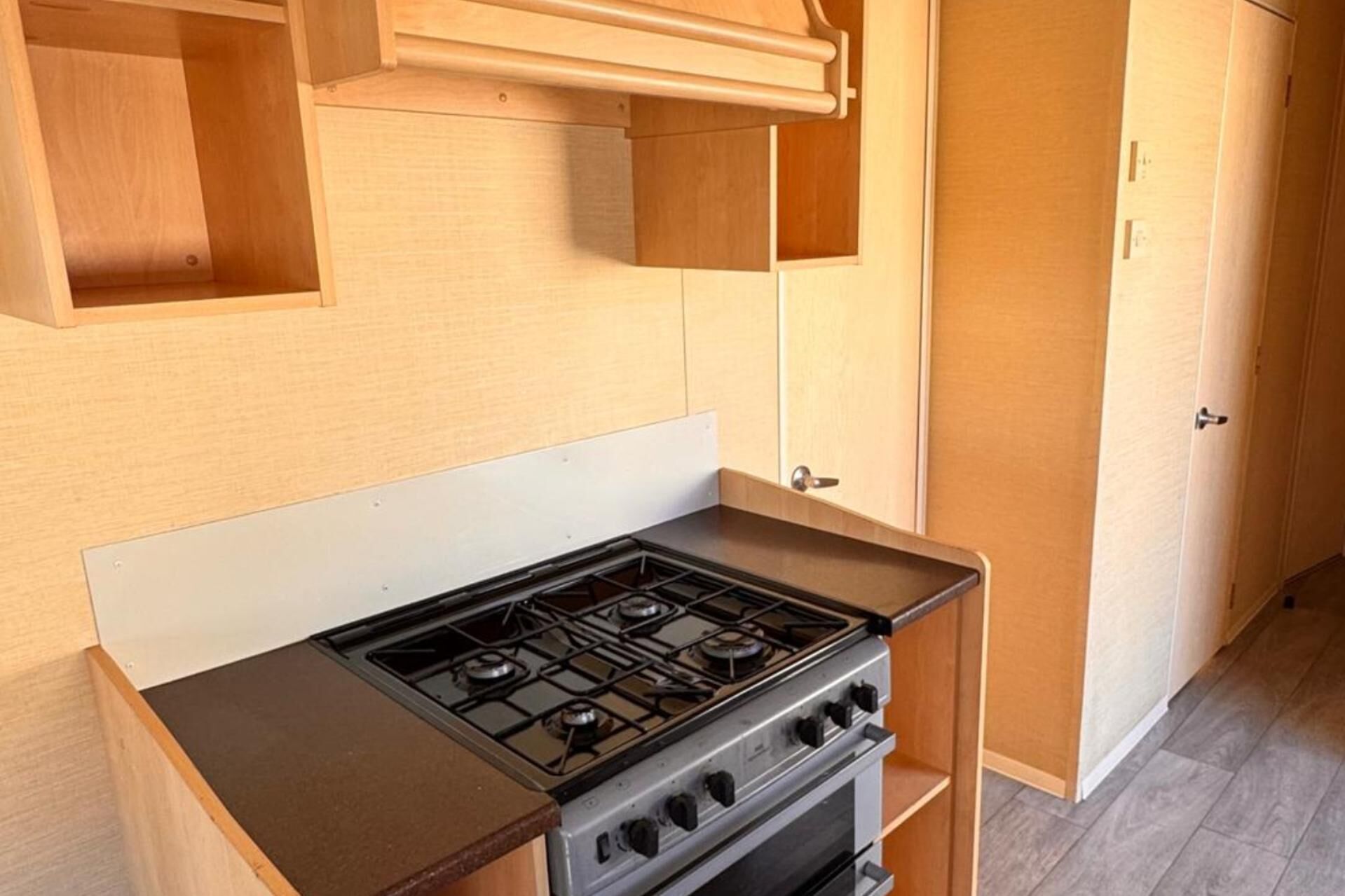 A compact kitchen with a gas stove, a built-in oven, and wooden cabinetry.