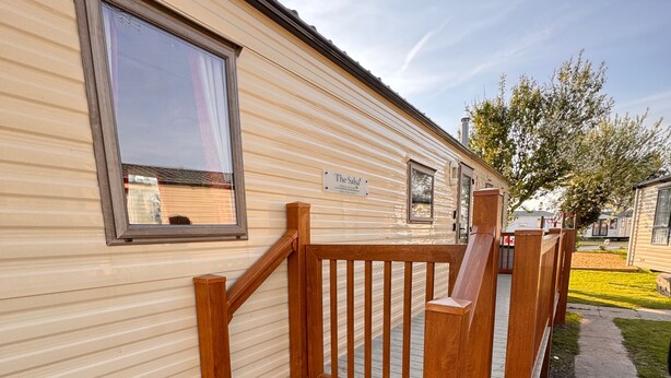 Una casa móvil con una escalera de madera que conduce a una terraza, una ventana y un letrero que dice "The Sal's".