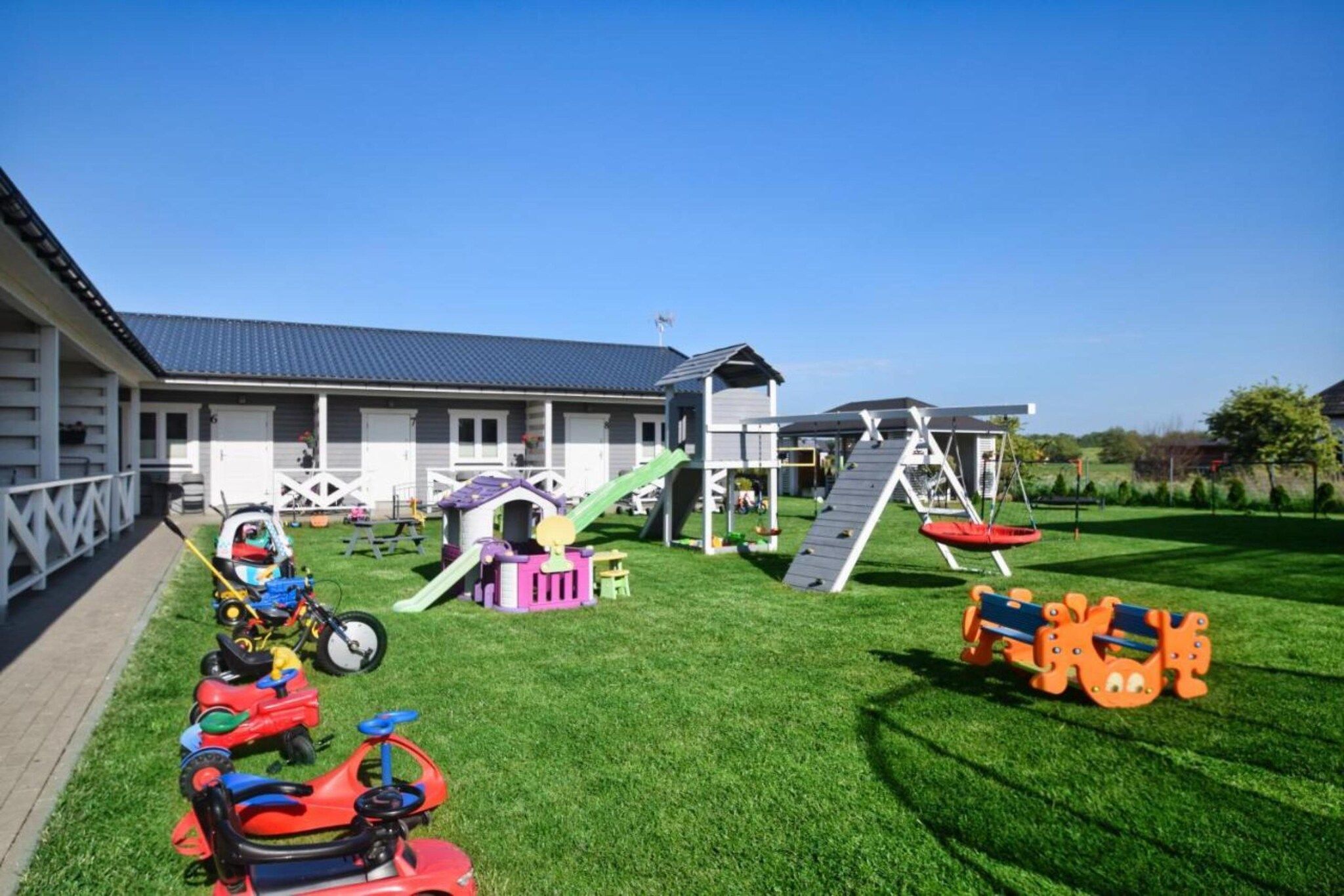 A residential property with a well-maintained lawn, a play area with a slide and climbing structures, and a garage.