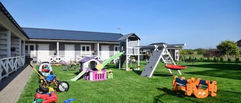 A residential property with a well-maintained lawn, a play area with a slide and climbing structures, and a garage.