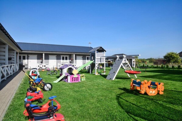 Une propriété résidentielle dotée d’une pelouse bien entretenue, d’un espace de jeux avec un toboggan et des structures d’escalade, ainsi que d’un garage.