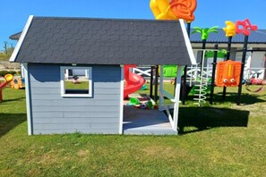 A small playhouse with a grey roof and a window, surrounded by a grassy area. - Holiday homes close to the beach, large playground (Sarbinowo)
