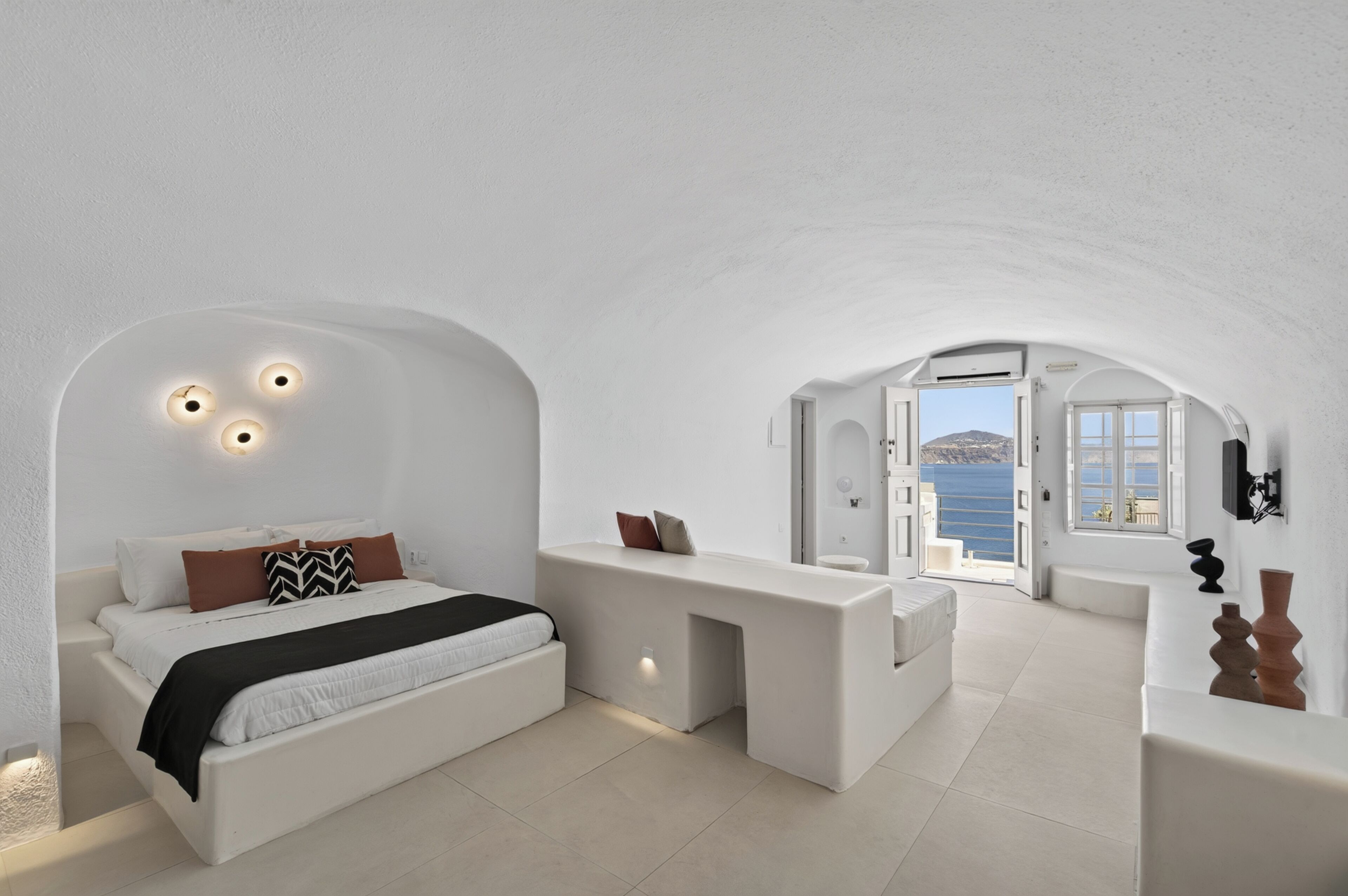 Un dormitorio moderno con decoración blanca, una cama, mesitas de noche y vistas al mar.