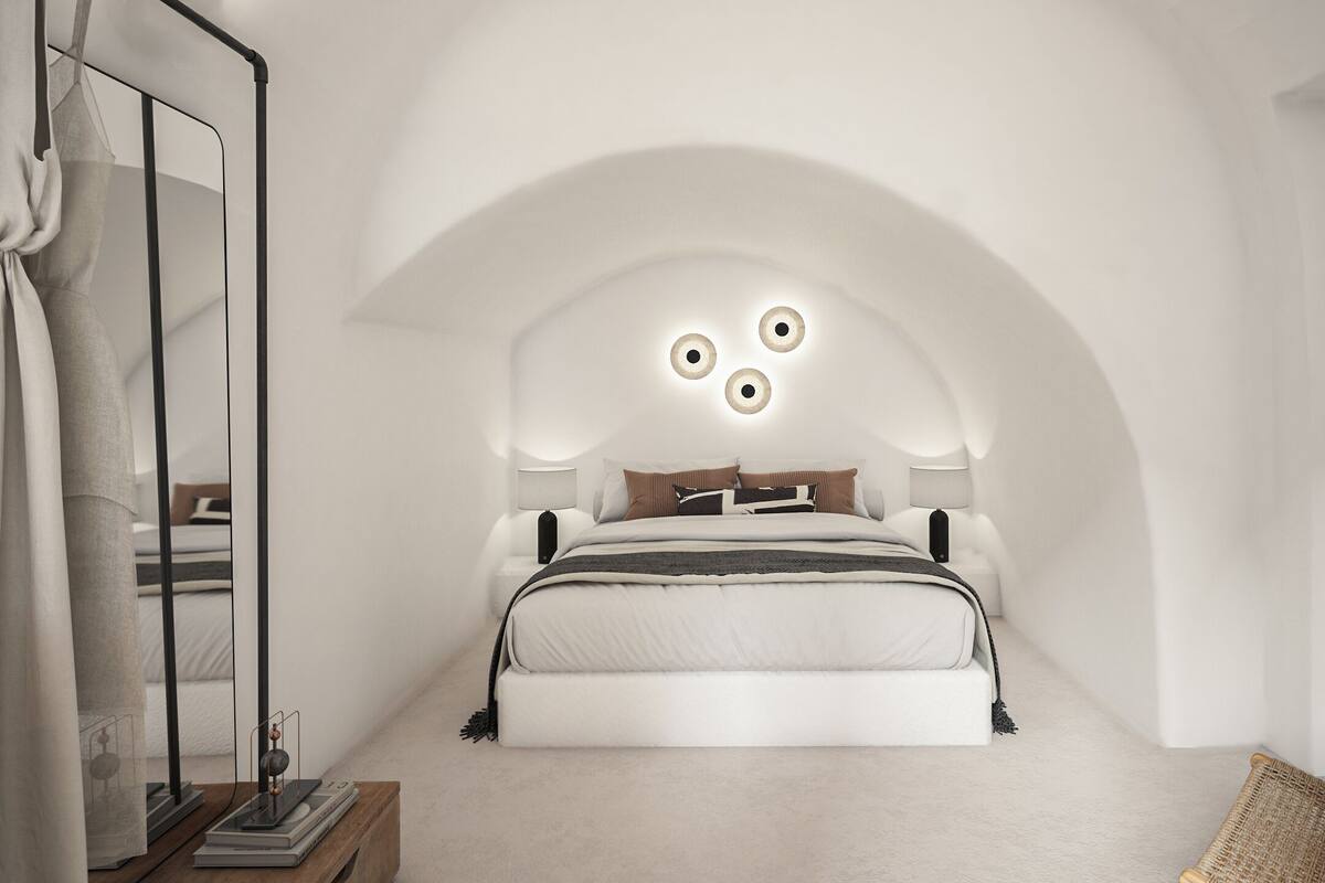 A modern bedroom with a curved ceiling, a large bed, bedside lamps, and a small table with books.