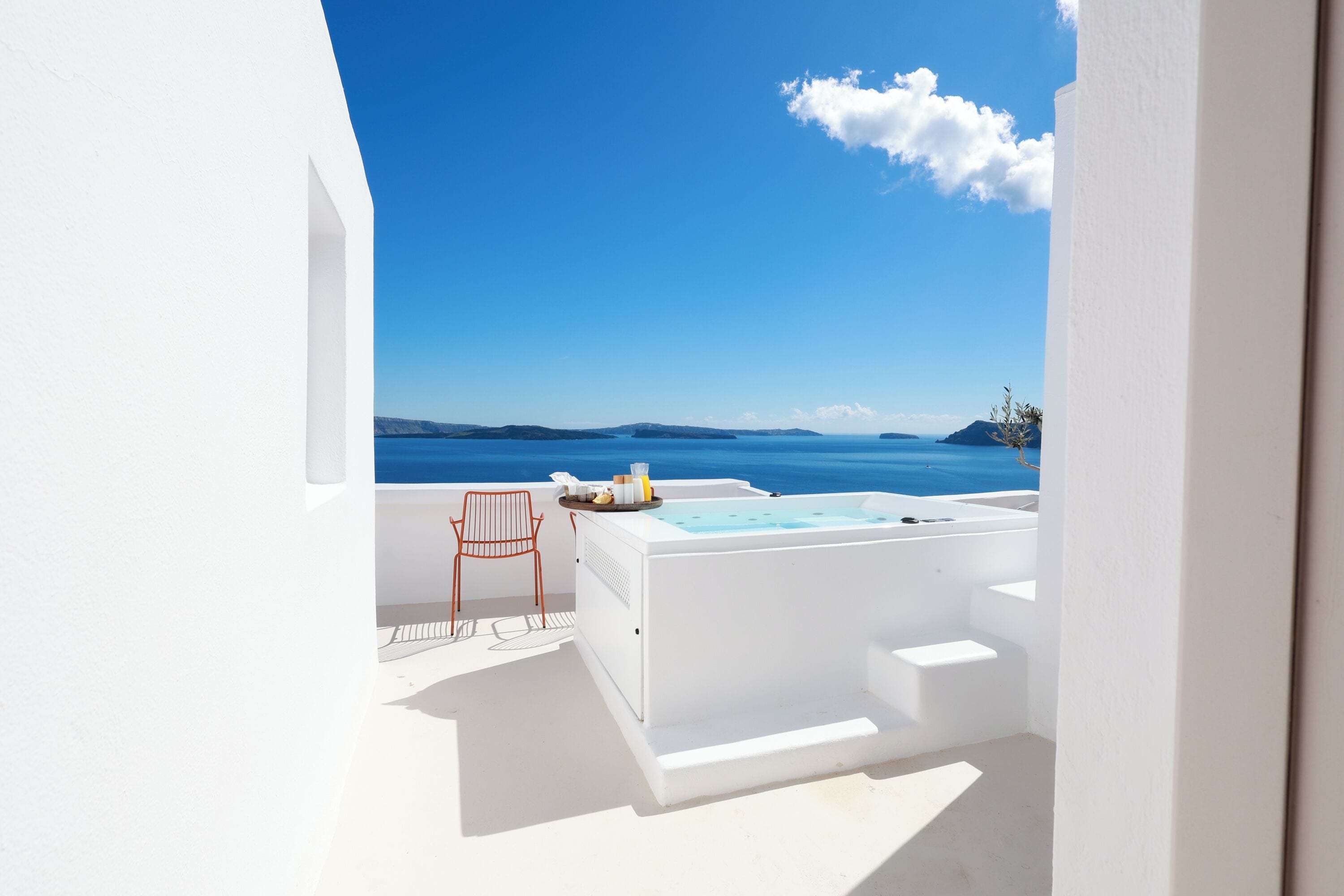 A white outdoor seating area with a hot tub, a chair, and a view of the sea.
