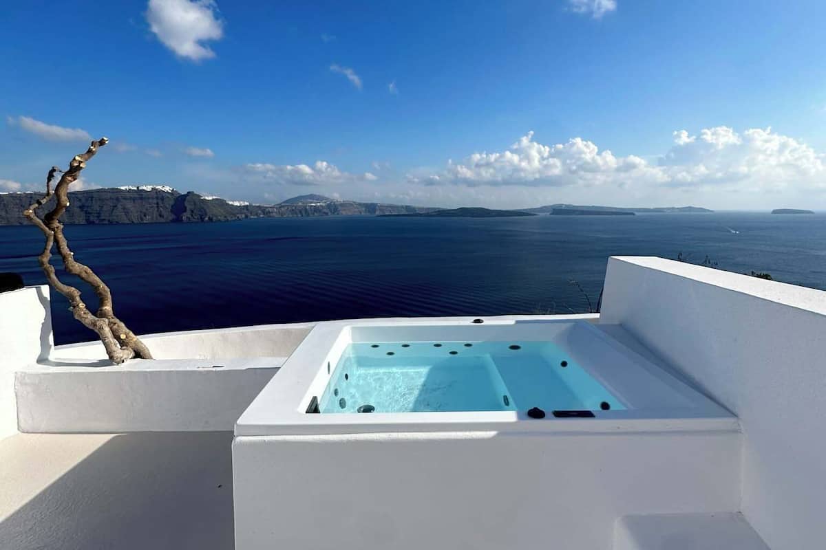A hot tub on a white deck with a view of the sea and distant land.