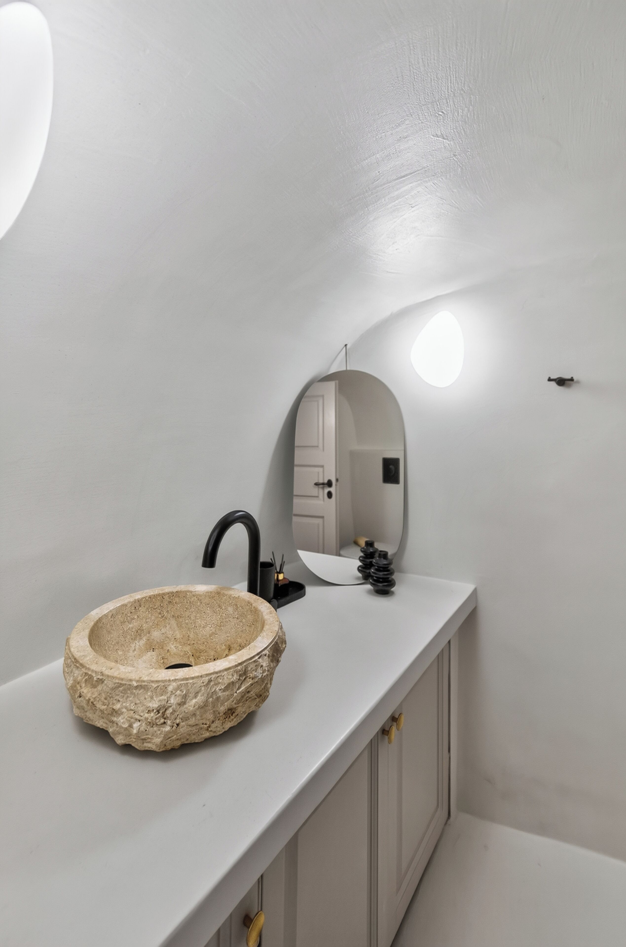 Une salle de bain moderne avec un lavabo en pierre, un robinet noir et un miroir rond.