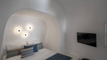 Een moderne slaapkamer met een gebogen plafond, een bed met opvallende kussens, een nachtkastje en een tv aan de muur.