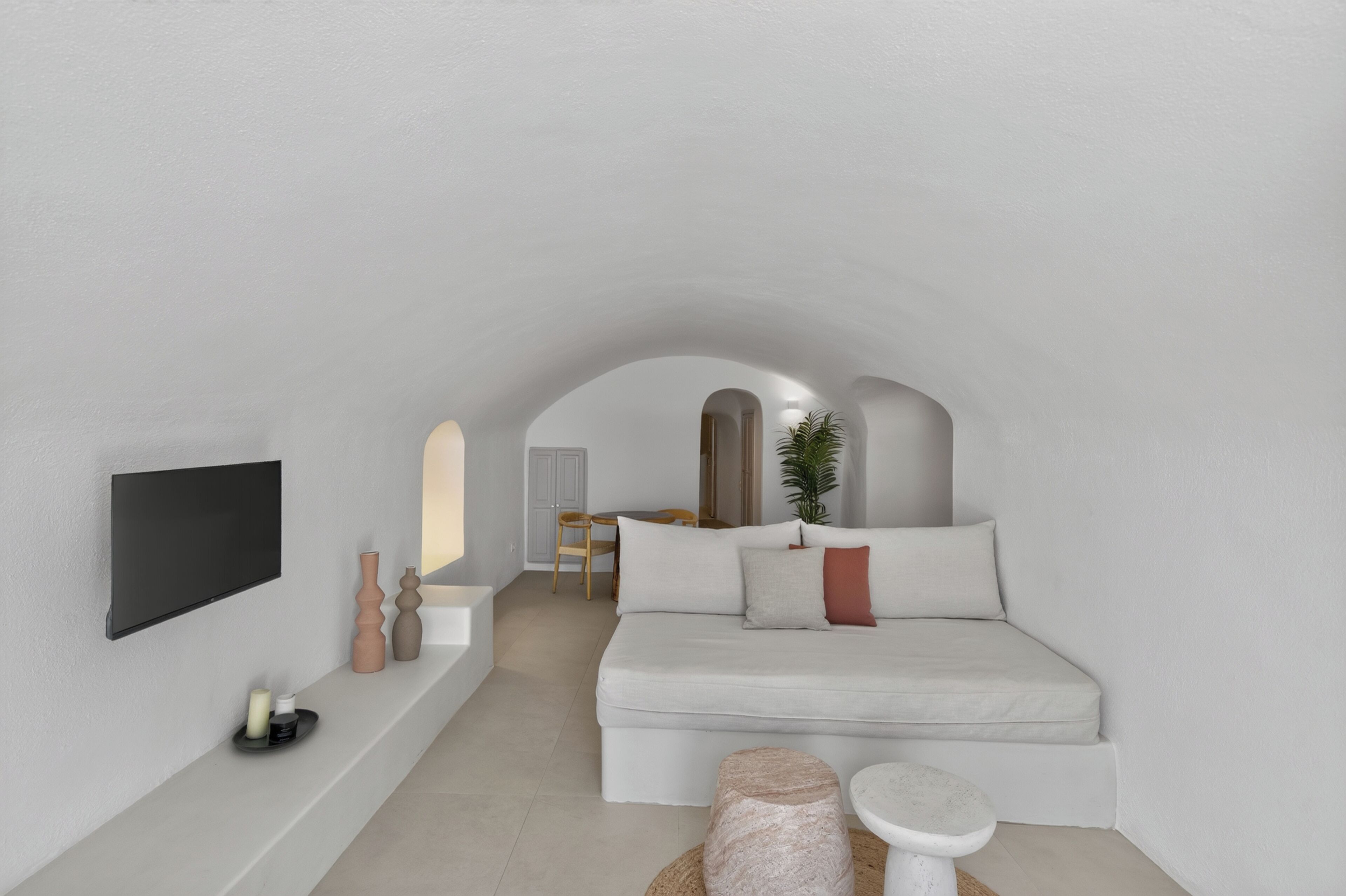 A minimalist room with a bed, a small table, a TV, and a plant.