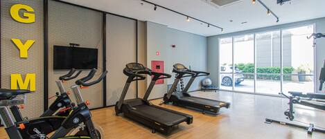 Un gimnasio con cintas de correr, bicicletas estáticas y un televisor en la pared.
