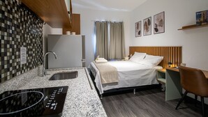 A modern hotel room with a kitchenette, a bed with a wooden headboard, a desk, and a chair. - Cozy Studio in Sao Paulo Sp-a713 (Sao Caetano do Sul)