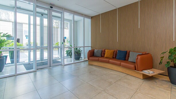 A modern lobby with a leather sofa, a wooden side table, and a large potted plant. - Cozy Studio in Sao Paulo Sp-a713 (Sao Caetano do Sul)