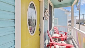 Une véranda avec deux fauteuils Adirondack rouges et une porte jaune ornée d’un vitrail décoratif.