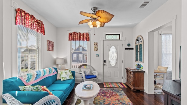 Un salon chaleureux avec un canapé de couleur turquoise, des fauteuils en osier, une table basse blanche et un ventilateur de plafond.
