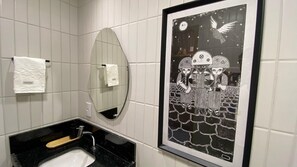 A bathroom with white tiled walls, a black sink, a mirror, and a framed black and white artwork depicting a bird and two figures. - Simple by Hosppedar (João Pessoa)