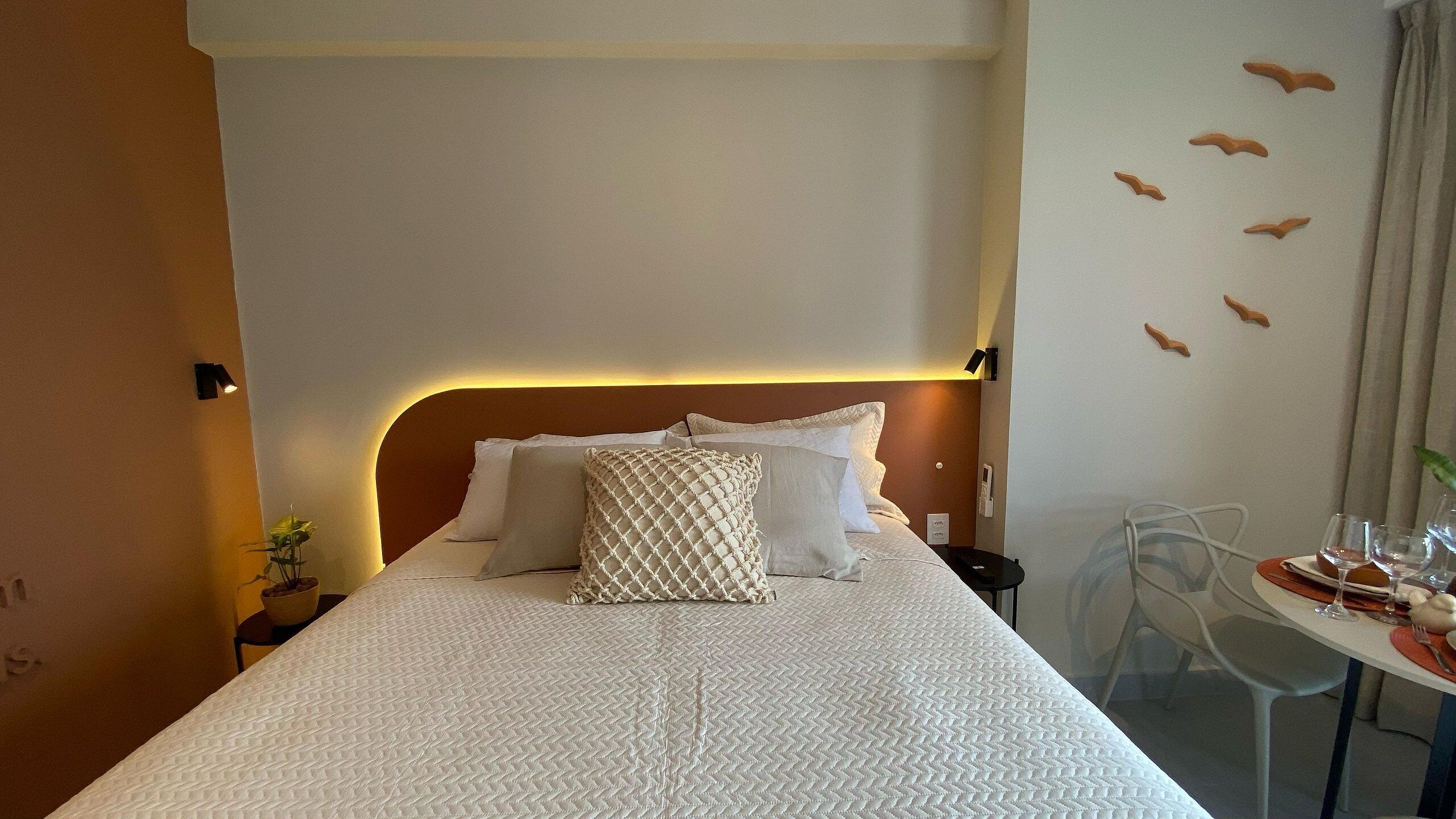 Una camera d'albergo con un letto rifatto, un comodino con una lampada e un'area pranzo con sedie e un tavolo apparecchiato per due persone.